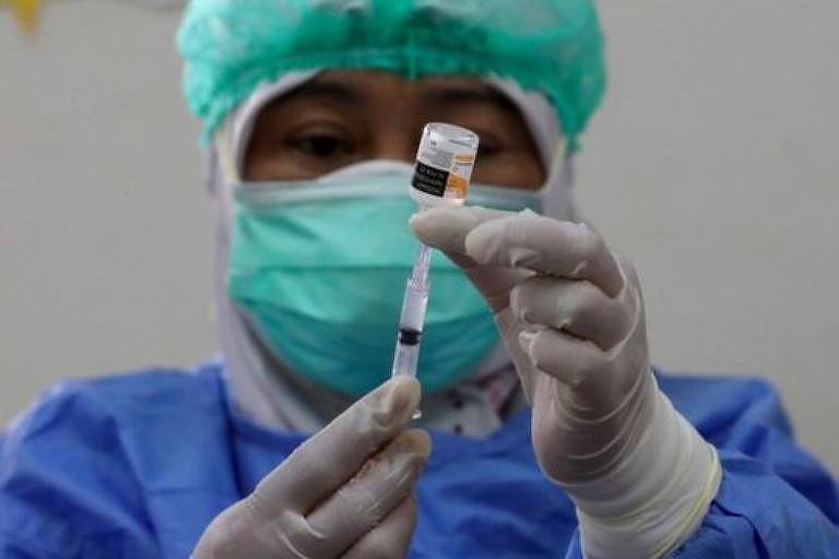 Profissional da sáude espeta uma seringa em uma ampola de vacina
