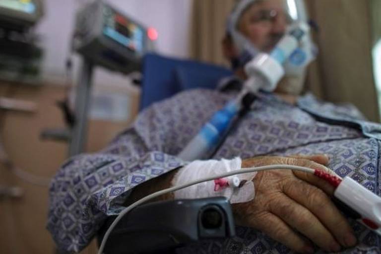 Homem idoso em uma sala de hospital está sentado e usa respirador