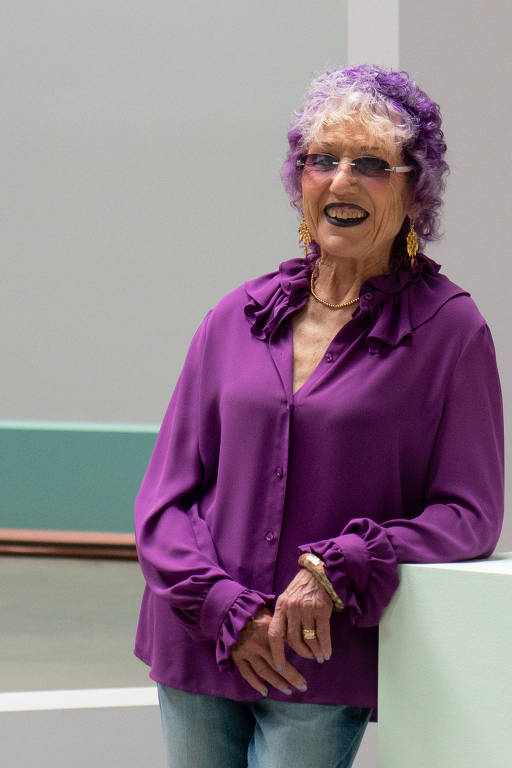 Retrato de mulher de 80 anos; ela veste camisa e óculos roxos e tem cabelo colorido