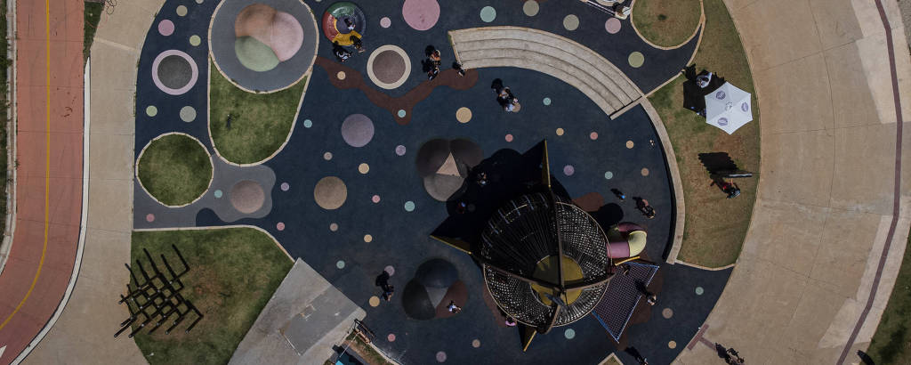 Vista aérea de parque onde há um foguete e uma espécie de planetário no chão, além de pessoas caminhando ao redor