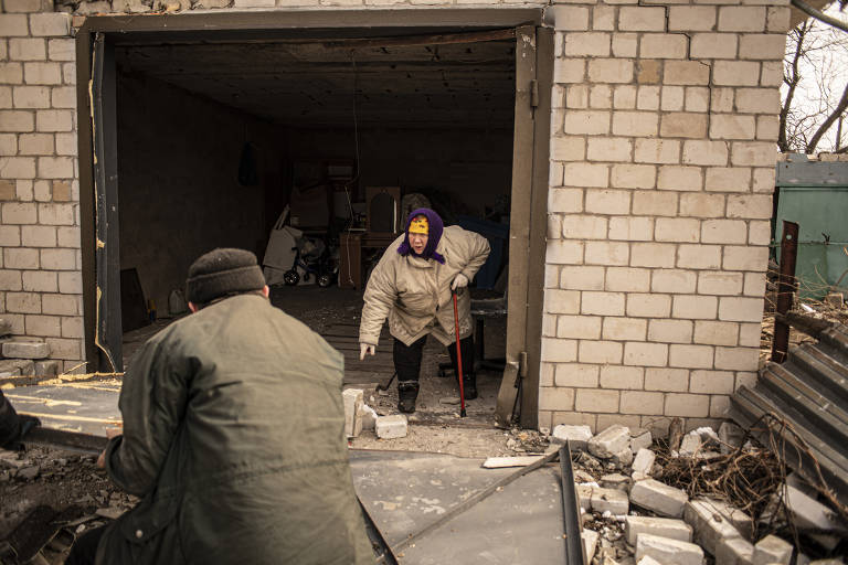 Mulher tenta recuperar utensílios da garagem de sua casa depois que o local foi bombardeado por tropas russas