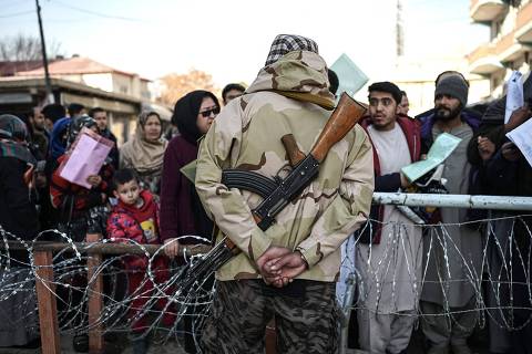 TOPSHOT - A Taliban fighter stands guard as people queue to enter the passport office at a checkpoint in Kabul on December 18, 2021. (Photo by Mohd RASFAN / AFP)