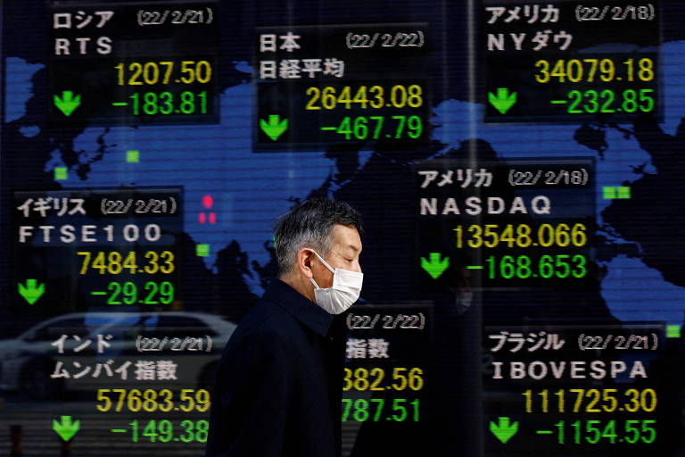 Homem passa diante de quadro eletrônico da Bolsa de Tóquio, no Japão, que mostra flutuação de índices de ações em diversas partes do mundo