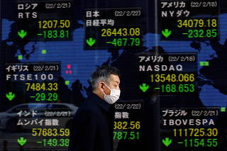 FILE PHOTO: A man wearing a protective mask, amid the coronavirus disease (COVID-19) outbreak, walks past an electronic board displaying Japan's Nikkei index and various countries' stock market index prices outside a brokerage in Tokyo