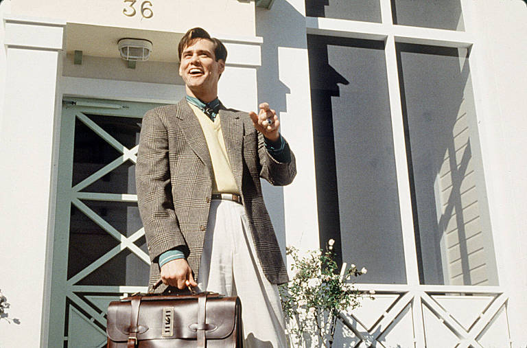 Carrey em frente à porta da casa do personagem, sorri e cumprimenta os vizinhos em cena do filme