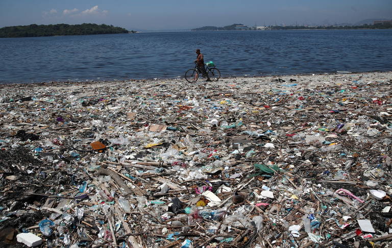Homem passa por praia poluída com plástico na baía de Guanabara, no Rio de Janeiro