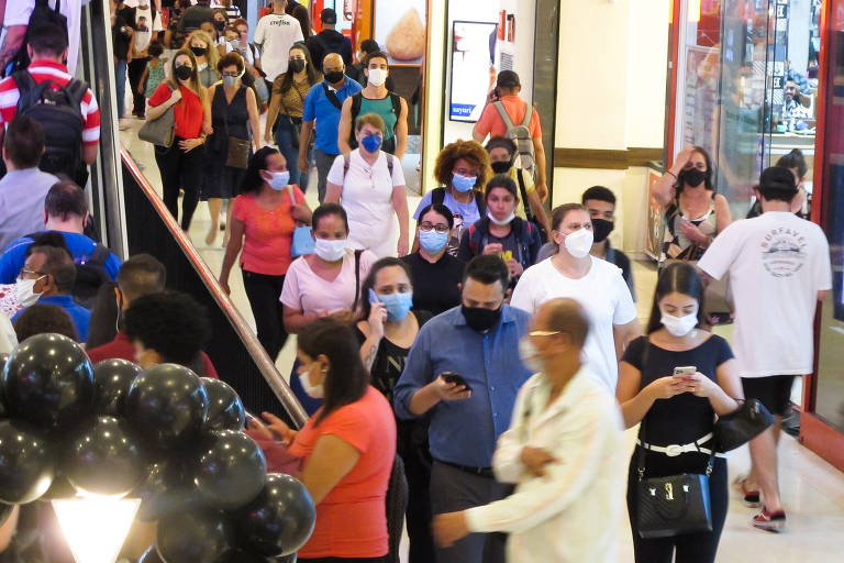 Pessoas caminham com e sem máscara em corredor de shopping