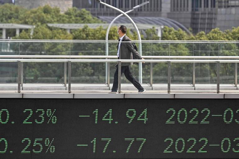 Homem passa sobre ponte com painel eletrônico que apresenta indicadores financeiros das ações negociadas em Xangai, na China
