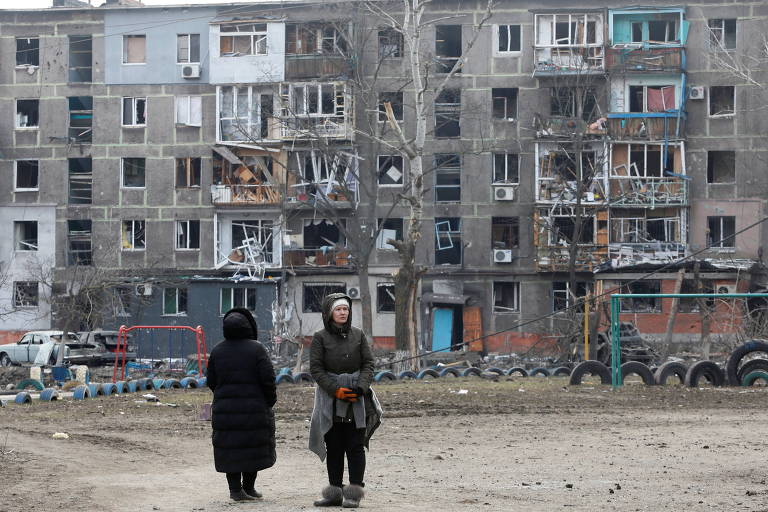 Moradores observam edifício residencial danificado após ataques na cidade de Mariupol, região oeste da Ucrânia