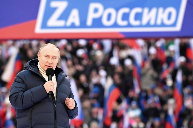Putin discursa com a frase "Pela Rússia" ("Za Rossiu") em um telão, usando o Z em letra latina indicando o símbolo da invasão russa da Ucrânia
