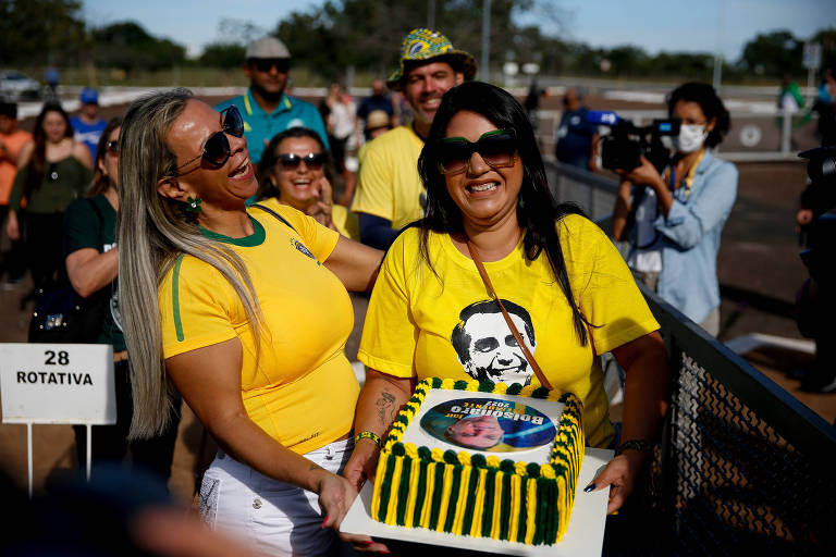 Mulheres de amarelo seguram bolo com a foto de Jair Bolsonaro estampada na cobertura