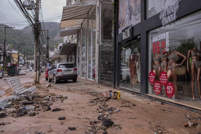 Foto de rua com lama no chão, galhos e folhas caídos e fachadas de lojas sujas