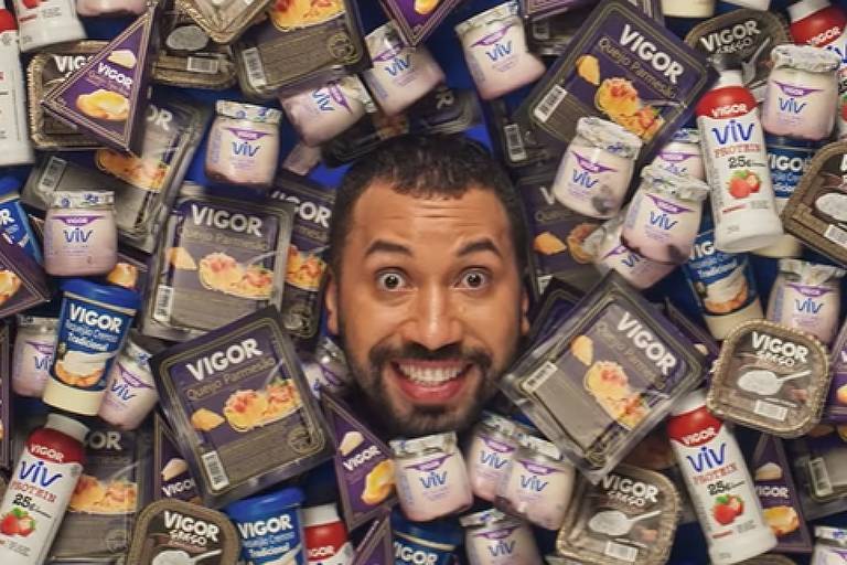Gil do Vigor aparece com rosto no centro da imagem em meio a diversas embalagens de iogurtes da Vigor