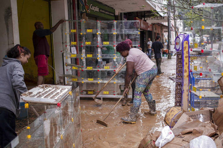 Mulher retira lama de loja após forte chuva que atingiu Petrópolis, no Rio de Janeiro