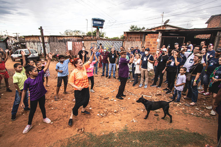 crianças dançam em favela, há um cachorro e adultos de plateia