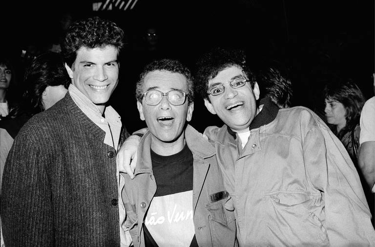 Foto em preto e branco, três homens brancos sorriem para a foto