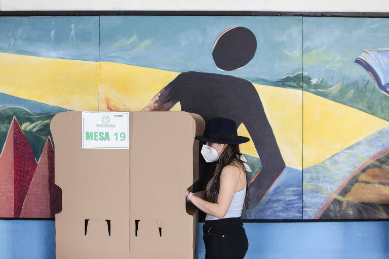 Mulher usando chapéu preto e máscara branca vota em Bogotá nas eleições legislativas da Colômbia