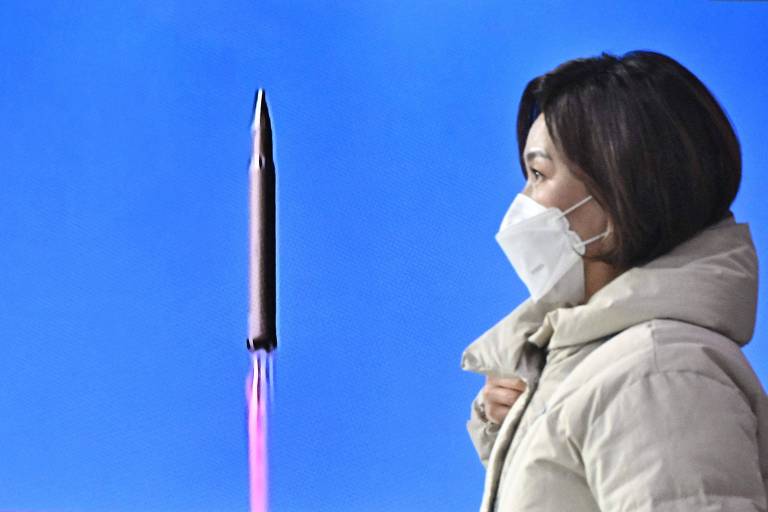 Mulher em Seul passa por tela de TV sintonizada em noticiário do lançamento do míssil pela Coreia do Norte, na estação de trem da capital sul-coerana 
