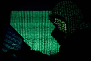 FILE PHOTO: Hooded man holds a laptop computer as cyber code is projected on him in this illustration picture