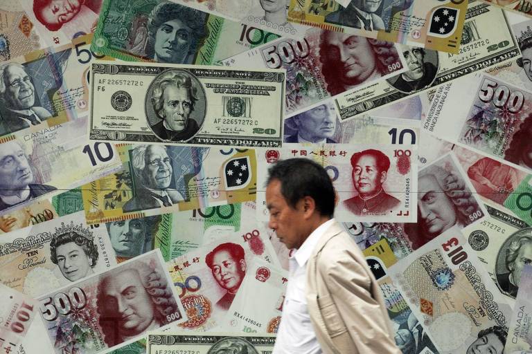 Homem passa por cartaz promocional de uma casa de câmbio em que mostra reproduções de cédulas de dólar, yuan e euro, em Hong Kong (China)