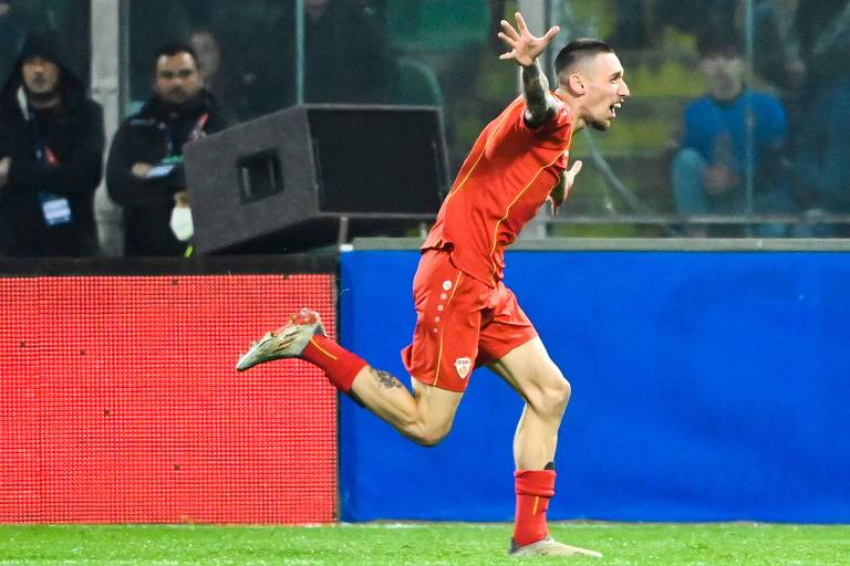 Trajkovski, atacante da Macedônia do Norte, corre com os braços abertos para comemorar gol contra a Itália nas Eliminatórias da Copa do Mundo; o uniforme dele é vermelho