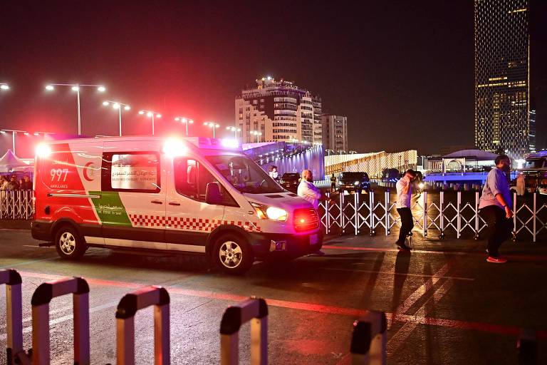 Fotografia colorida mostra ambulância com luzes vermelhas ligadas, em uma via de acesso, durante à noite na cidade de Jidá