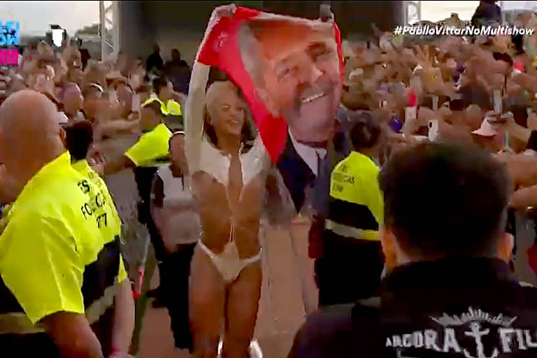 Imagem reproduzida de vídeo mostra a cantora Pabblo Vittar andando ao lado do público, abaixo do palco de seu no show no festival Lollapalooza. A cantora segura uma toalha de banho que tem a figura do ex-presidente Lula estampada