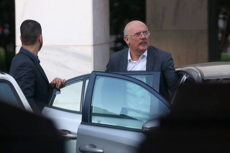 ex-ministro Milton Ribeiro (Educação) é flagrado saindo do carro enquanto um homem segura a porta, em meio a movimentação de automóveis no local; duas pilastras brancas são vistas ao fundo. 