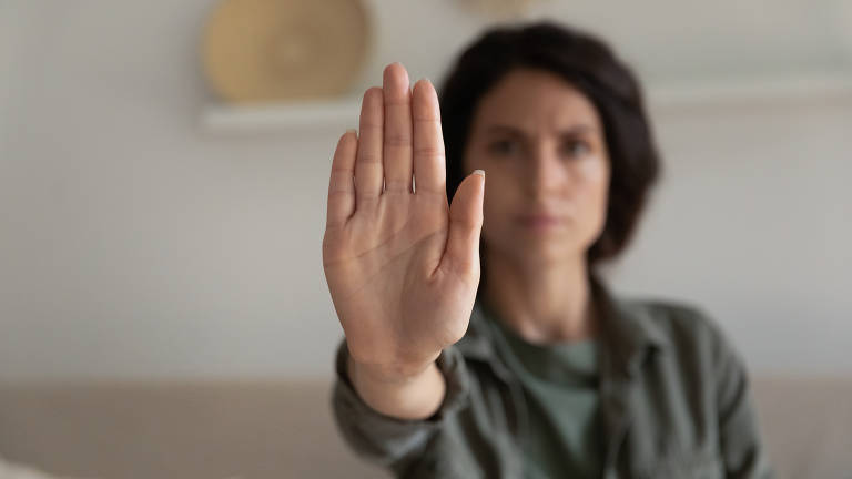 Imagem mostra mulher fazendo o sinal de "pare" com a mão.
