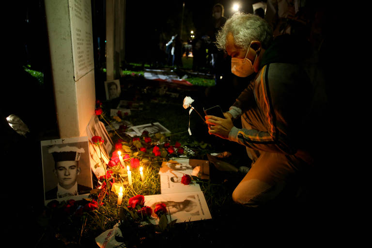 Uma pessoa acende uma vela no meio das fotos de vitimas da ditadura militar.