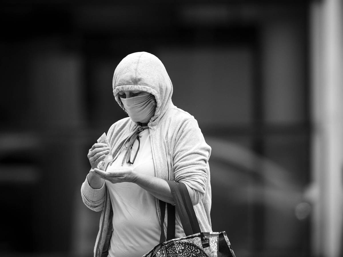Mulher na avenida Paulista passa álcool em gel nas mãos, durante o primeiro dia de uso obrigatório de máscaras protetoras faciais na cidade de São Paulo, em 7.mai.2020 