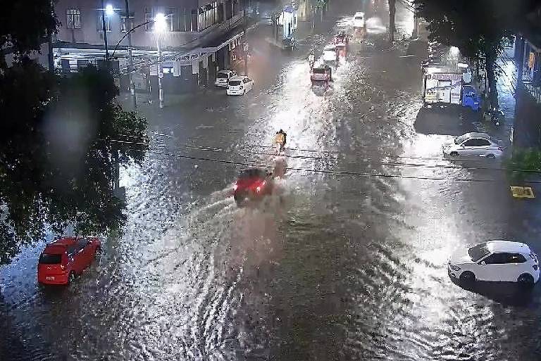 A imagem mostra carros passando em uma rua alagada por causa da chuva no Rio de Janeiro