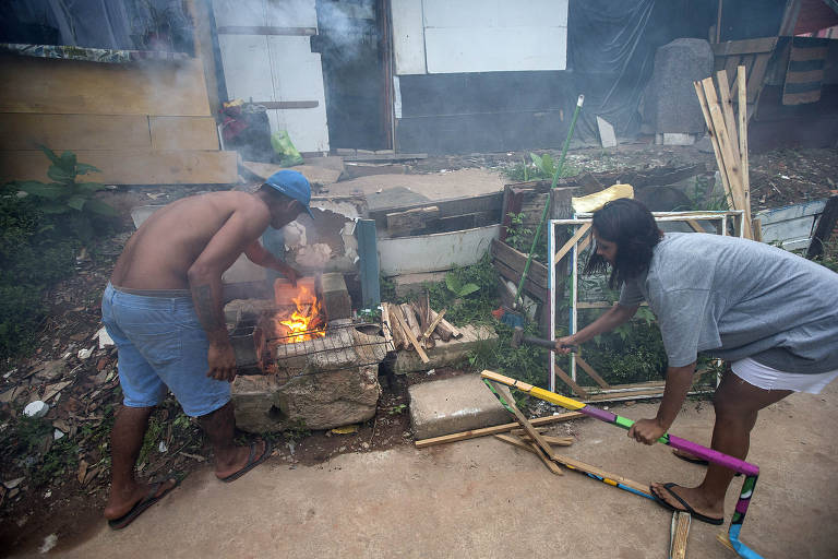 Moradores de ocupação em São Paulo acendem fogão a lenha improvisado com madeiras recolhidas da rua.