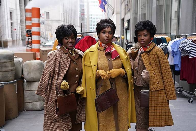 Três mulheres negras, uma ao lado da outra, posam para foto; todas usam casacos
