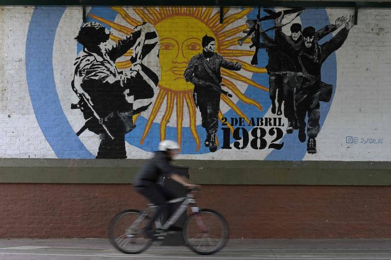 Homem anda de bicicleta, em Buenos Aires, ao lado de um mural que retrata foto icônica da rendição de fuzileiros britânicos na guerra das Malvinas