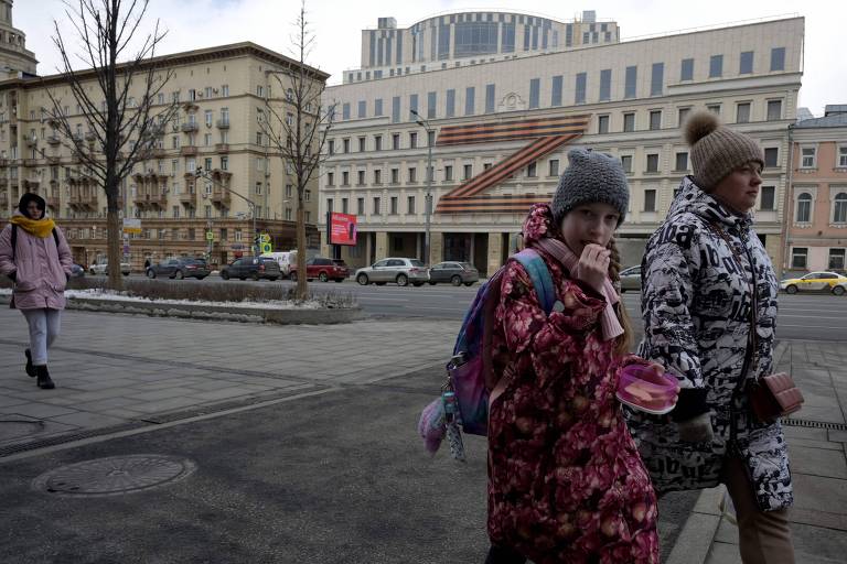 Pedestres em frente a teatro adornado com a letra 'Z', um dos símbolos russos da guerra, em Moscou