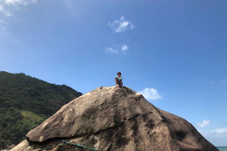 Menino sentado no topo de uma grande pedra