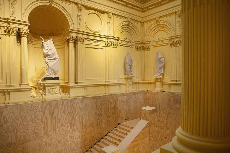 Vista interna do museu, com destaque para a escadaria que dá acesso ao andar superior, onde diversas estátuas estão localizadas. Elas estão cobertas por um pano.