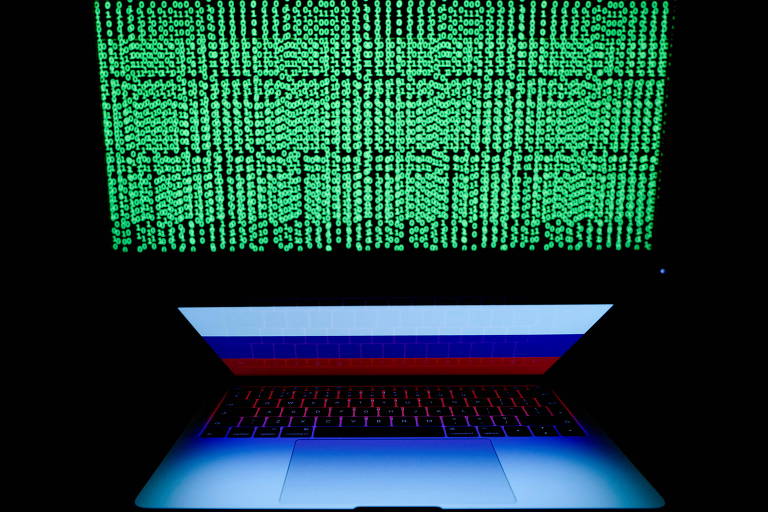 Uma bandeira russa é vista na tela do laptop em frente a uma tela de computador na qual o código cibernético é exibido