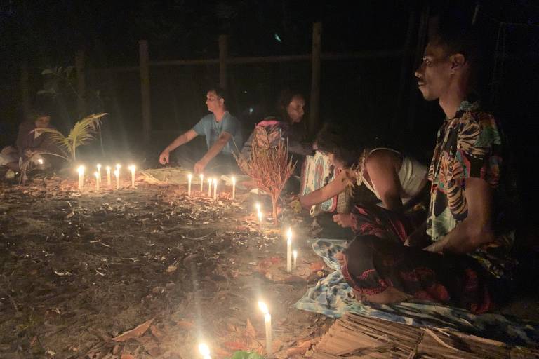 Pessoas sentadas ao redor de círculo de velas acesas