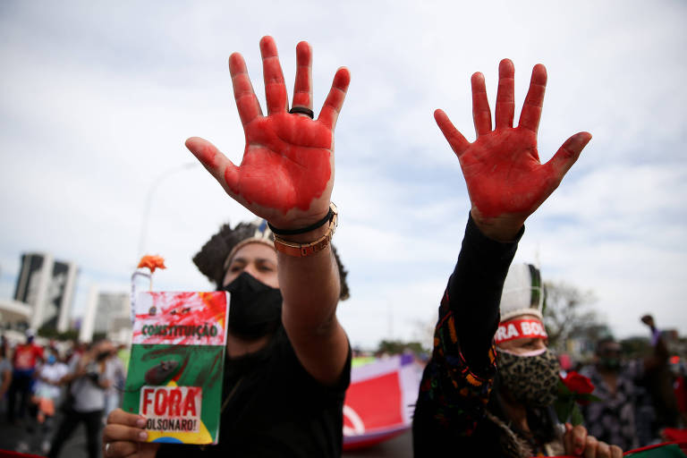 Manifestantes com as mãos pintadas de vermelho em dia de céu claro seguram exemplar da Constituição