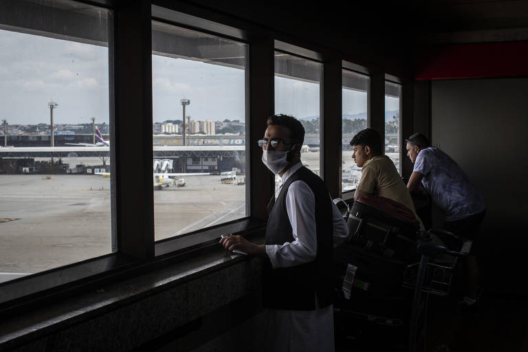 Hekmat Ullah e Ahmad Shinwari olham pela janela com vista da pista do aeroporto