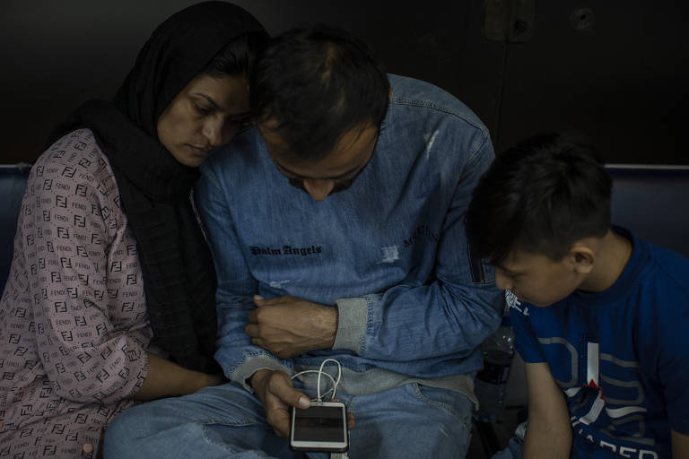 Mohammad Zahim Nasimi, 31, e sua esposa, Khalida, 28, utilizam o telefone conectado à rede wi-fi do aeroporto ao lado do filho mais velho
