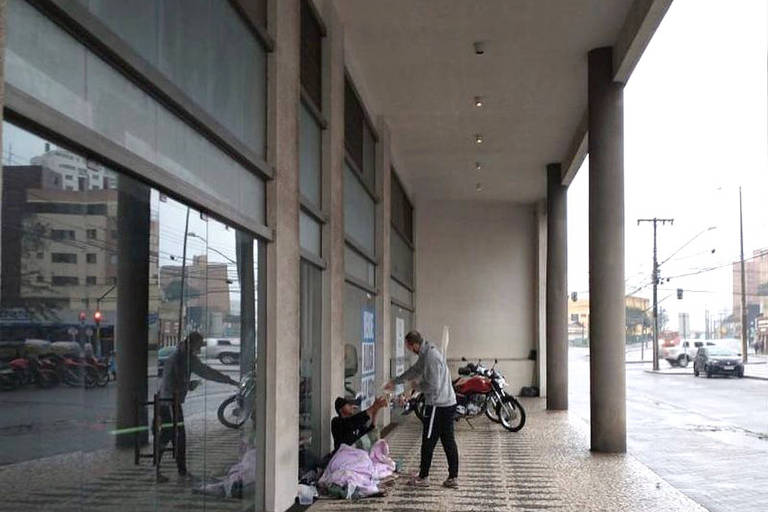 homem entrega refeição a pessoa deitada na calçada com cobertor
