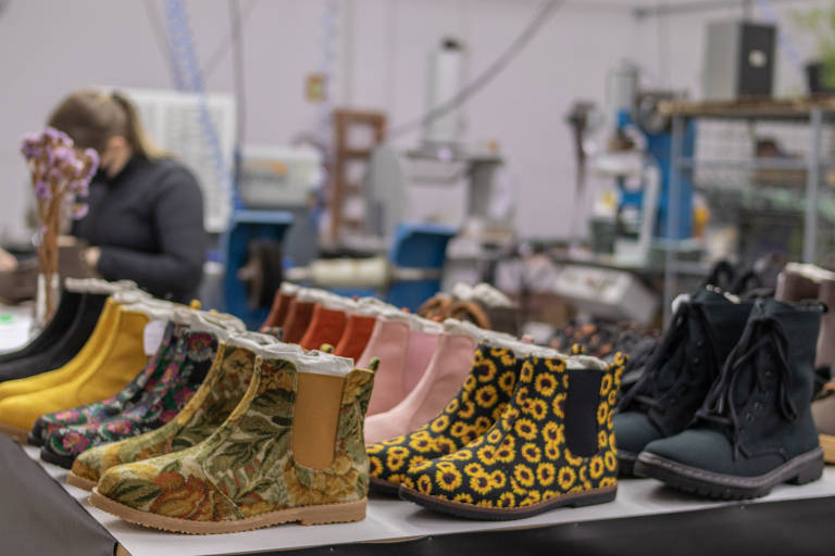 Linha de produção de sapatos veganos em fábrica; há calçados pretos, cor-de-rosa e com estampas amarelas, por exemplo