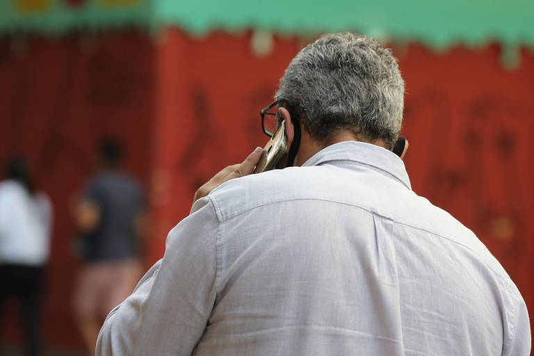 Homem de cabelos brancos fala ao celular de costas para a câmera
