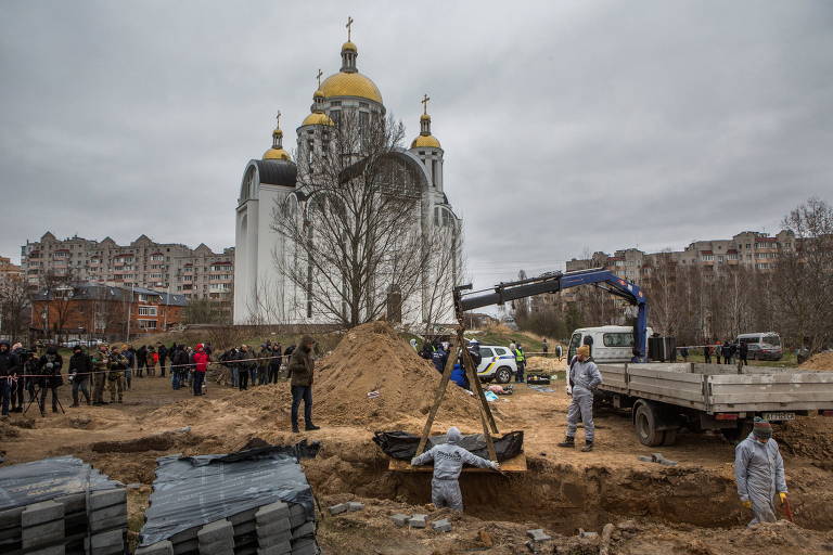 Técnicos com uniformes que cobrem todo o corpo erguem cadáver embalado em saco preto; ao fundo, aparece uma  grande igreja com três cúpulas douradas, no estilo das igrejas ortodoxas russas. 