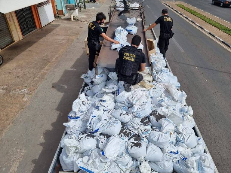 Dois policias federais observam caminhão com carga de cassiterita ilegal apreendida em Boa Vista (RR)