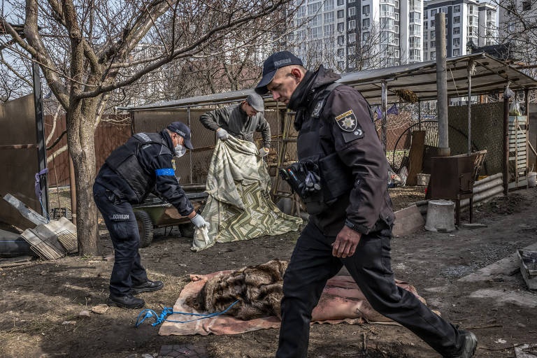 Policiais cobrem corpo de mulher encontrado em porão em Butcha, nos arredores de Kiev