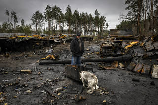 A man and his dog look at the destroyed Russian tanks and other debris on a forest road near Dmytrivka, Ukraine, on April 2, 2022. (Ivor Prickett/The New York Times)